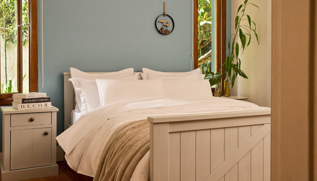 Quarto de hotel aconchegante com cama arrumada, lençóis brancos e decoração natural, transmitindo conforto e hospitalidade.