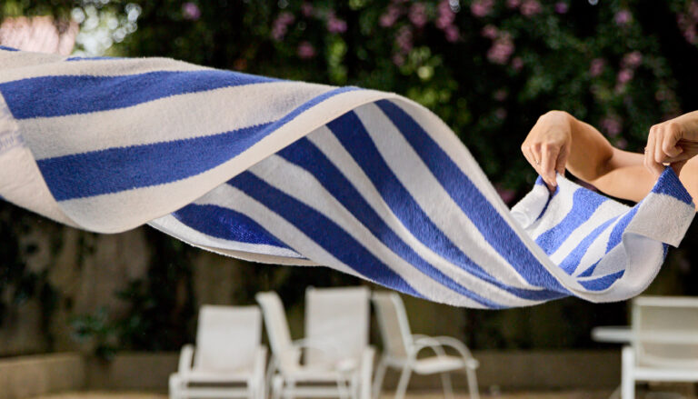 Toalha de piscina listrada azul e branca sendo sacudida ao ar em área externa de hospedagem.