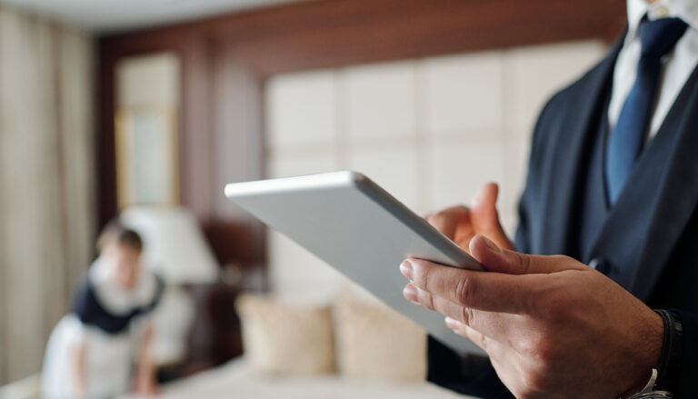 Profissional de hotelaria usando tablet em quarto de hotel, avaliando checklist de enxoval para alta temporada de verão