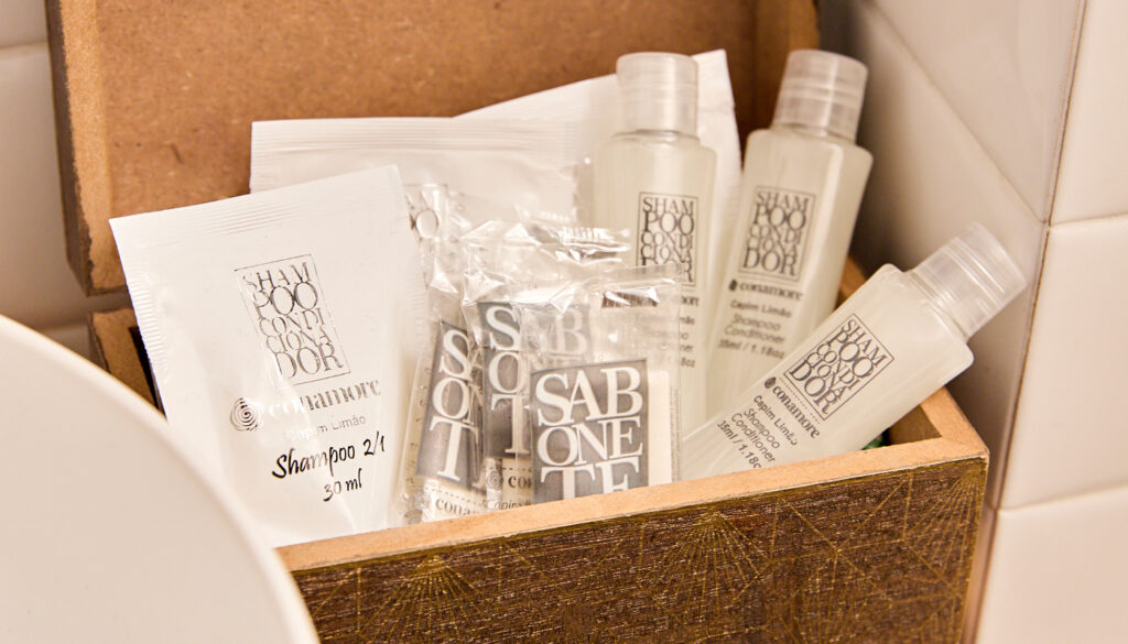 Kit de amenities para hotelaria com sabonete e shampoo Conamore organizados em caixa no quarto
