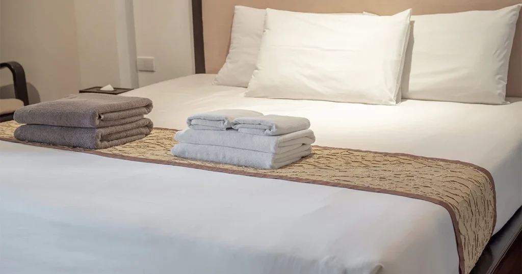 Cama de hotel com enxoval branco e toalhas organizadas para hospedagem
